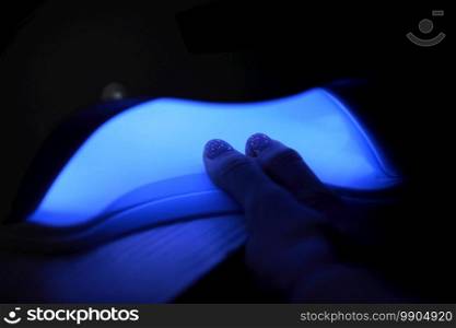 Closeup view of female hands with gel polish manicure. Woman puts hand into led uv l&for curing top cover of nailpolish. UV l&, LED Nail.. Closeup view of female hands with gel polish manicure. Woman puts hand into led uv l&for curing top cover of nailpolish. UV l&, LED Nail