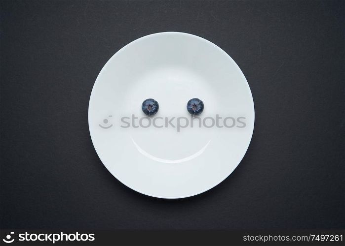 Closeup view of fresh two blueberry on white disc ,black background , smile and happy morning breakfast concept