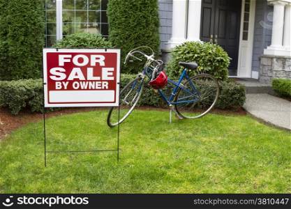 Closeup view of Modern Suburban Home with for Sale Real Estate Sign in front yard and bicycle and house in background