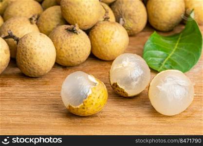 Closeup view of peeled longan and pile of the whole with green leaf on wooden table.