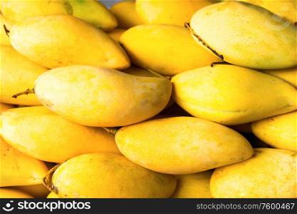Closeup view of pile of fresh ripe yellow mango fruits at market stall. Can be used as healthy food background
