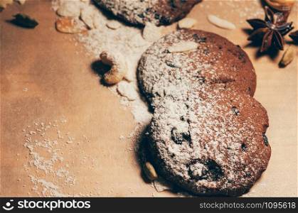 Closeup view of round crunchy chocolate cookies with nuts, cocoa chips and spices, on textured paper background, with flours on top