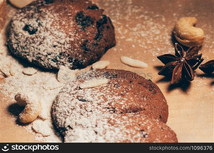 Closeup view of round crunchy chocolate cookies with nuts, cocoa chips and spices, flour on top, on textured paper background