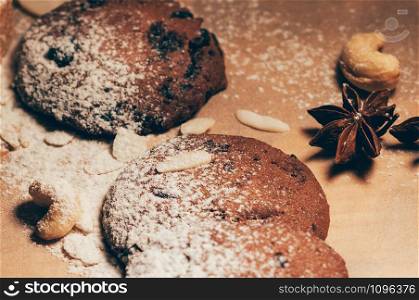 Closeup view of round crunchy chocolate cookies with nuts, cocoa chips and spices, flour on top, on textured paper background