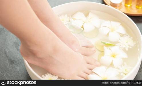 closeup view of woman soaking her feet in dish with water and flowers on wooden floor. Spa treatment and product for female feet and hand spa. white flowers in ceramic bowl.