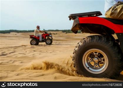 Closeup view on atv wheel, man in helmet on background. Male person on quad bike, sandy race, dune safari in hot sunny day, 4x4 extreme adventure, quad-biking. View on atv wheel, man in helmet on background