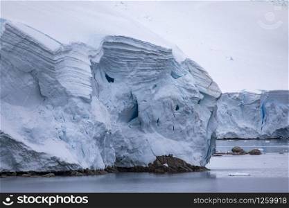 Closeup with icicles on huge glacier tongue with meter-high ice and snow on sea shore