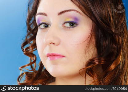 Closeup woman face, girl with long brown curly hair colorful makeup portrait on blue