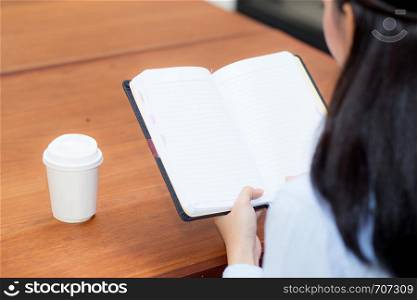 closeup woman hand writing on notebook on wooden table, girl work with paper at coffee shop, top view; freelance business concept.