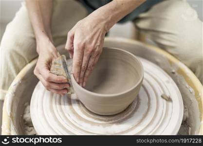 Closeup woman hands making clay pot in workshop. Unrecognized artist sculpting from wet clay in studio. Unknown female ceramist doing handmade product in pottery. Hands of young woman working on pottery wheel in cozy workshop and making vase or mug