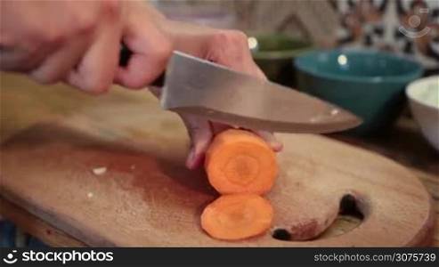 Closeup woman hands slicing fresh carrot on wooden cutting board
