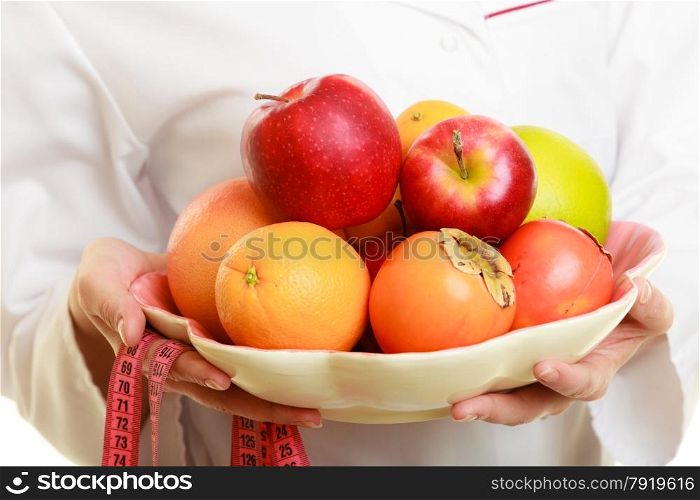Closeup woman in white lab coat holding fruits and colorful measure tapes isolated. Doctor dietitian recommending healthy food. Dieting