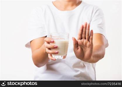 Closeup woman raises a hand to stop sign use hand holding glass milk she is bad stomach ache has bad lactose intolerance unhealthy problem with dairy food, studio shot isolated on white background
