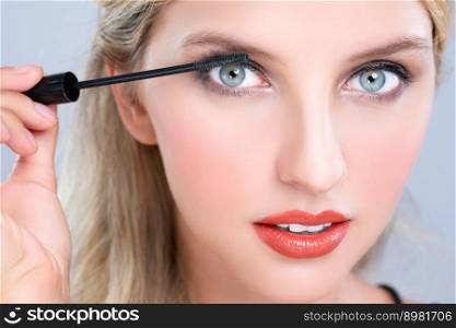 Closeup woman with blond hair putting alluring black mascara with brush in hand on long thick eyelash. Perfect fashionable cosmetic clean facial skin with beautiful eye young woman in high resolution.. Closeup beautiful woman putting alluring black mascara on long thick eyelashes.