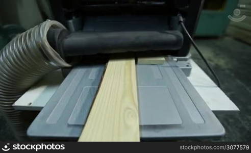 Closeup wooden boards going out of electric planing machine. Frontal view. Process of smoothing the surface of planks in carpentry workshop with electric planer.