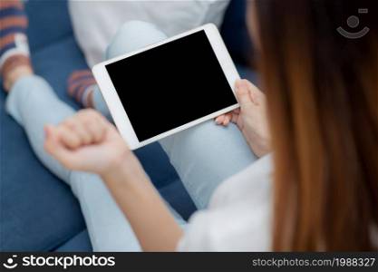Closeup young asian woman sitting and using mockup of tablet computer with display blank screen on sofa at home, girl holding digital tablet watch entertainment at living room, communication concept.