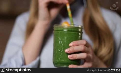Closeup young beautiful woman enjoying healthy raw vegetable juice. Middle section of female holding mason jar of fresh blended green smothie with striped straw and orange slice and drinking. Healthy eating and dieting.