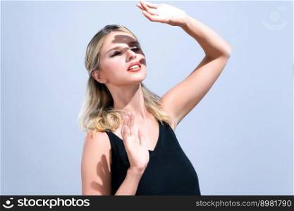 Closeup young blond hair woman with perfect skin and soft alluring facial makeup raise her hand cover her face from bright sunlight in isolated background for skincare sunscreen product.. Closeup young woman with alluring soft makeup cover face with hand.