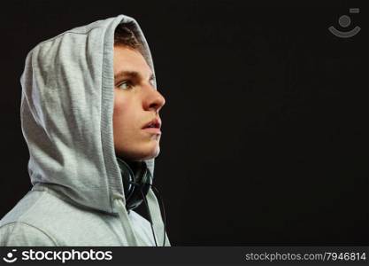 Closeup young handsome hooded man with headphones listening to music sideview dark background