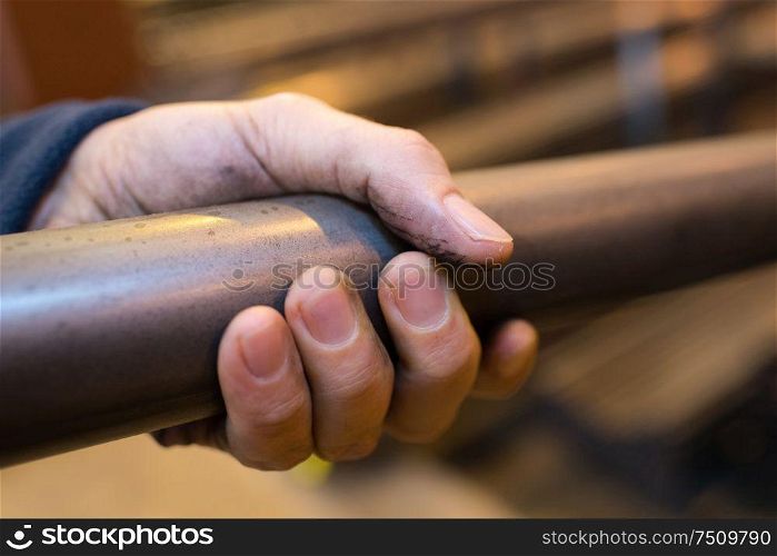 closup of male hand gripping metal tube in industrial factory