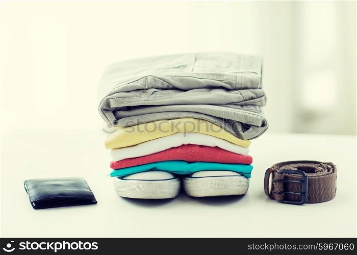 clothes and personal staff concept - close up of folded shirts, pants, belt, wallet and shoes on table at home