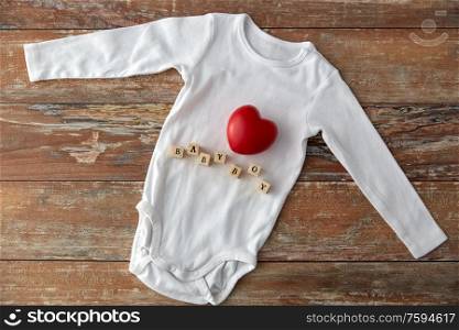 clothes, babyhood and clothing concept - bodysuit for baby boy with red heart and toy blocks on wooden table. baby boy&rsquo;s bodysuit with red heart on wooden table