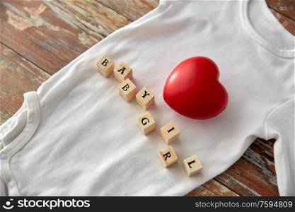 clothes, babyhood and clothing concept - bodysuit for baby girl with red heart and toy blocks on wooden table. baby bodysuit with red heart on wooden table