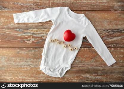 clothes, babyhood and clothing concept - bodysuit for baby girl with red heart and toy blocks on wooden table. baby bodysuit with red heart on wooden table