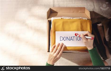 Clothes Donation Concept. Box of Cloth with Donate label. Woman Preparing Used Old Garment at Home. Top View