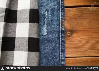 clothes, fashion and objects concept - close up of checkered shirt and jeans on wooden background