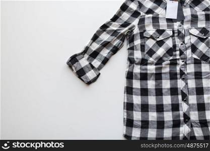 clothes, fashion and objects concept - close up of checkered shirt with price tag on white background