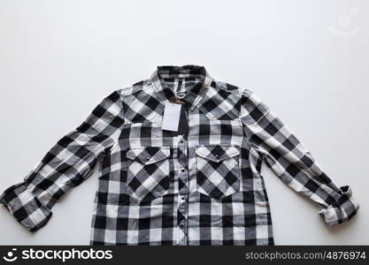 clothes, fashion and objects concept - close up of checkered shirt with price tag on white background