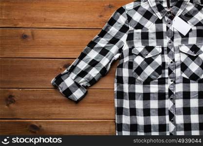 clothes, fashion and objects concept - close up of checkered shirt with price tag on wooden background. close up of checkered shirt on wooden background
