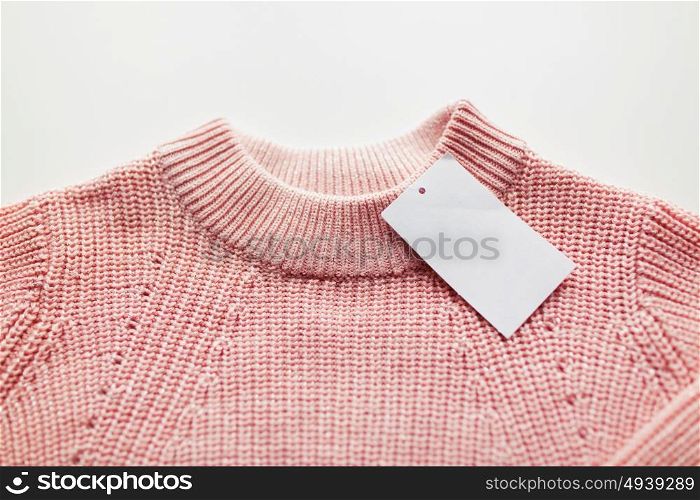 clothes, fashion and objects concept - close up of sweater or pullover with price tag on white background. close up of sweater or pullover with price tag