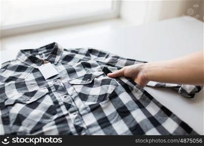 clothes, fashion, people and shopping concept - close up of hand holding checkered shirt with price tag