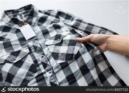 clothes, fashion, people and shopping concept - close up of hand holding checkered shirt with price tag. close up of hand and shirt with price tag