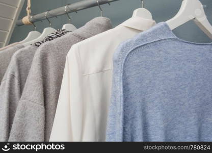 Clothes hang on a a clothing rack, white gray and blue, close-up. Clothes hang on a a clothing rack, white gray and blue,