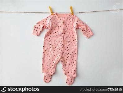 clothes, laundry, babyhood and clothing concept - pink long-sleeved bodysuit for baby girl with dot print hanging on clothesline with pins on white background. bodysuit for baby girl hanging on rope with pins