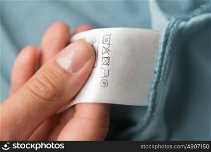 clothes, laundry, people and housekeeping concept - close up of hand holding label with users manual of clothing item. hand holding label with users manual of clothing