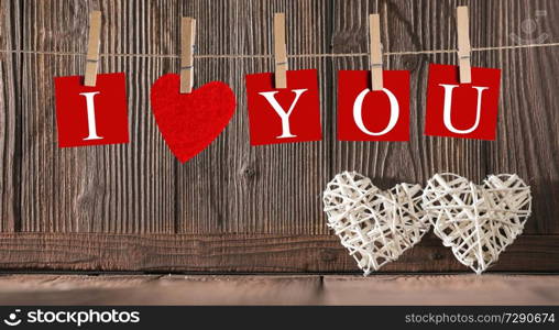 Clothes pegs and I LOVE YOU words on papers on rope on wooden background with wicker hearts Valentines day concept. Pegs and I LOVE YOU words on rope