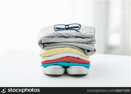 clothes, personal staff and objects concept - close up of folded shirts, pants, glasses and shoes on table at home