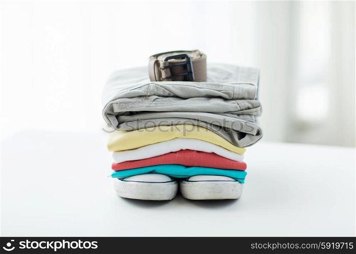clothes, personal staff and objects concept - close up of folded shirts, pants, belt and shoes on table at home