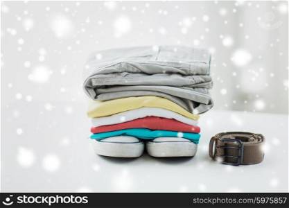 clothes, personal staff and objects concept - close up of folded shirts, pants, belt and shoes on table at home over snow effect
