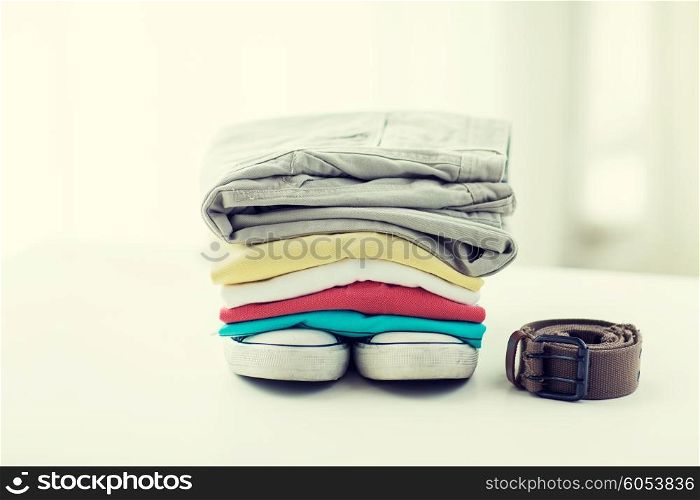 clothes, personal staff and objects concept - close up of folded shirts, pants, belt and shoes on table at home