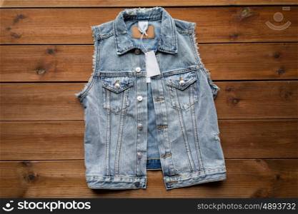 clothes, wear and fashion concept - close up of denim vest or waistcoat with price tag on wooden background