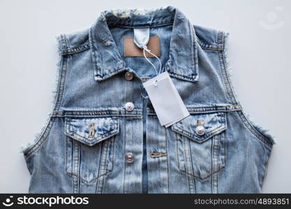 clothes, wear and fashion concept - close up of denim vest or waistcoat with price tag on white background