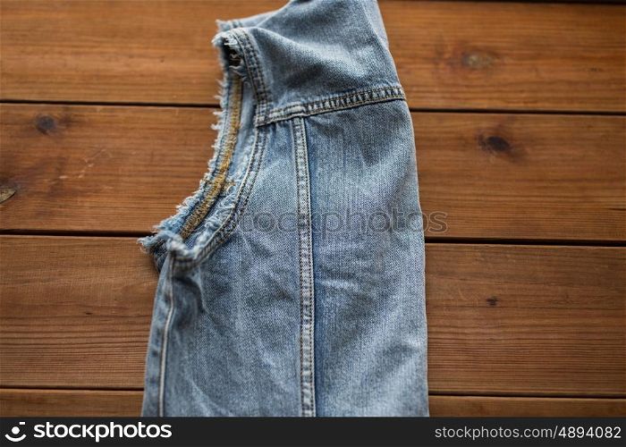 clothes, wear and fashion concept - close up of denim vest or waistcoat on wooden background