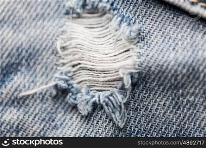 clothes, wear and fashion concept - close up ripped denim jeans with hole. close up of hole on shabby denim or jeans clothes