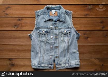 clothes, wear and fashion concept - denim vest or waistcoat on wooden background