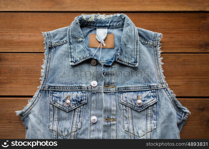 clothes, wear and fashion concept - denim vest or waistcoat on wooden background